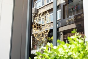 Un edificio con un logotipo geométrico en la puerta de vidrio, fachada de piedra y balcones con plantas.