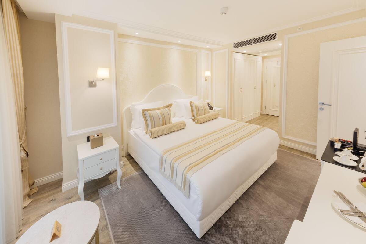 A hotel room with a large bed, a bedside table, a chair, and a desk with a chair.