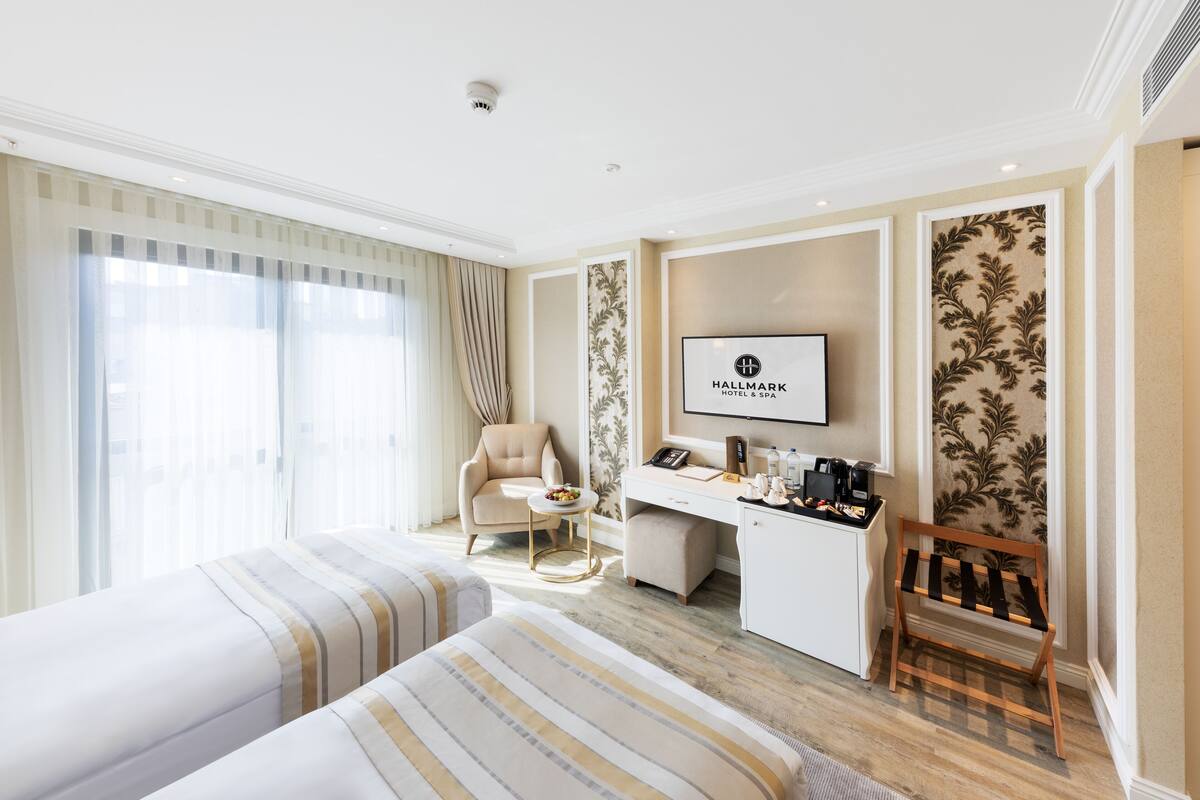 A hotel room with two beds, a desk, a chair, a television, and a coffee machine.