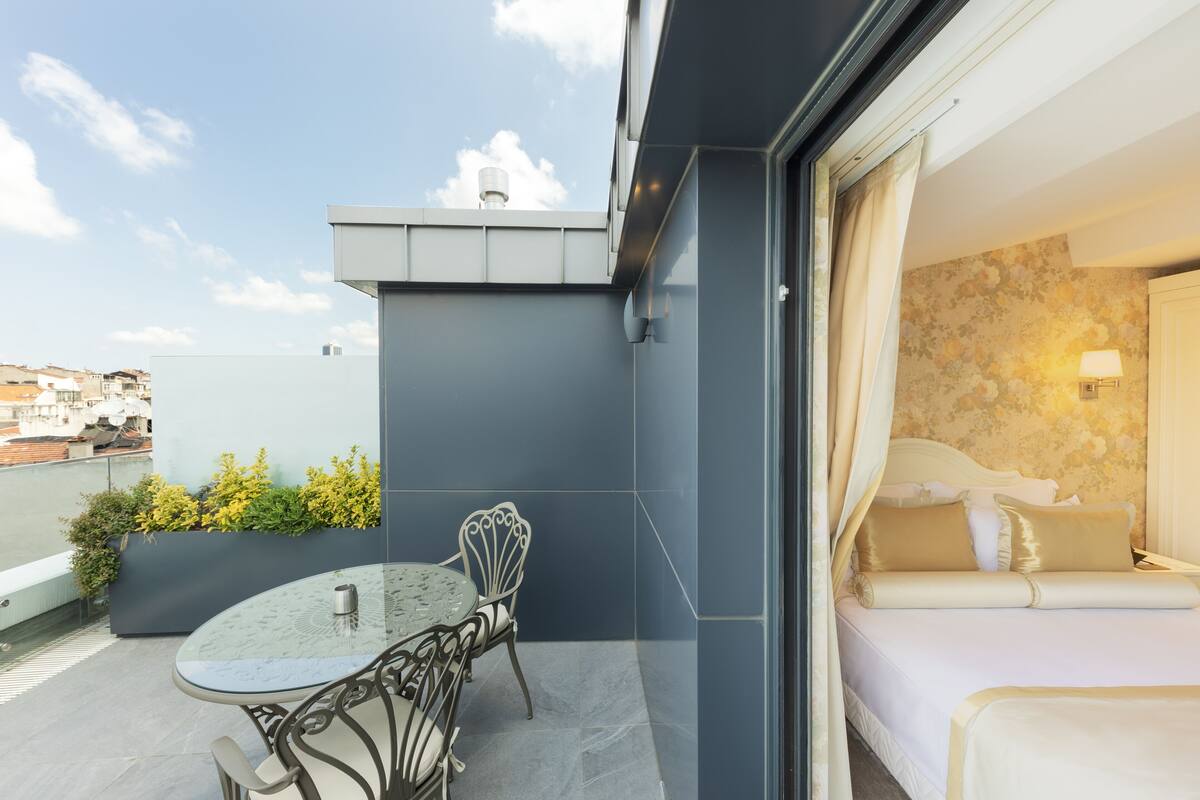 A modern hotel room with a balcony, a bed with white bedding, and a small table with chairs.