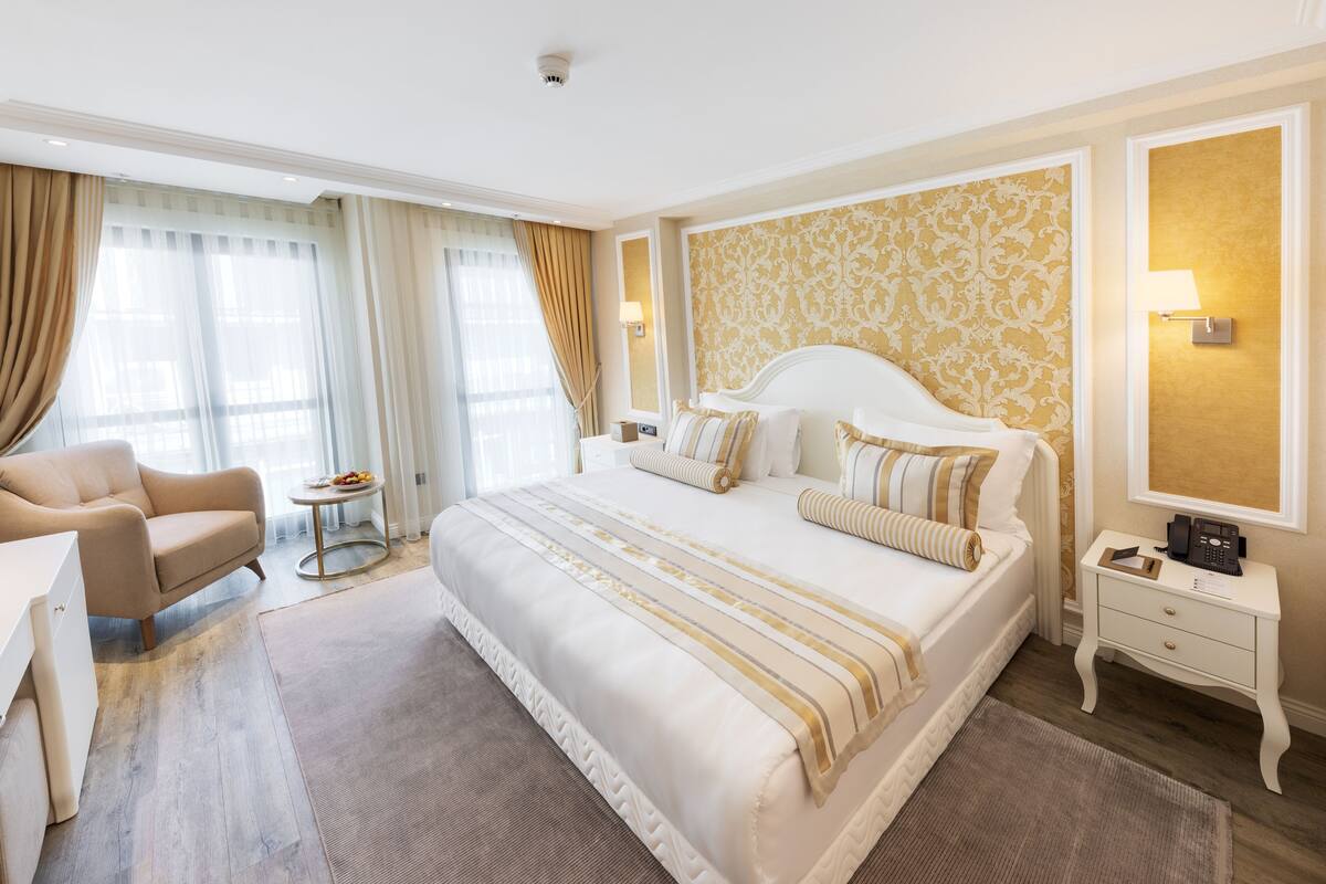 A spacious hotel room with a large bed, a bedside table, a chair, and a small round table.