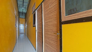 A corridor with yellow walls and wooden doors, leading to a room with a large window. - SPOT ON 91761 Ramah Tamah Homestay Syariah (Pekanbaru)