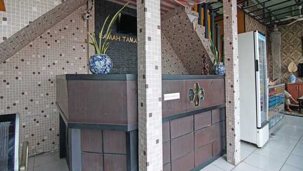 A reception area with a tiled wall, a reception desk, a sign reading "STOP SANDAL", and a refrigerator. - SPOT ON 91761 Ramah Tamah Homestay Syariah (Pekanbaru)