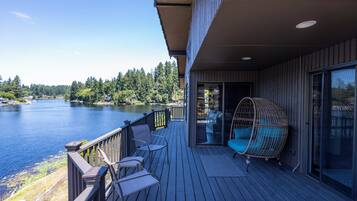 Une terrasse en bois avec des chaises et un fauteuil suspendu, donnant sur un lac.