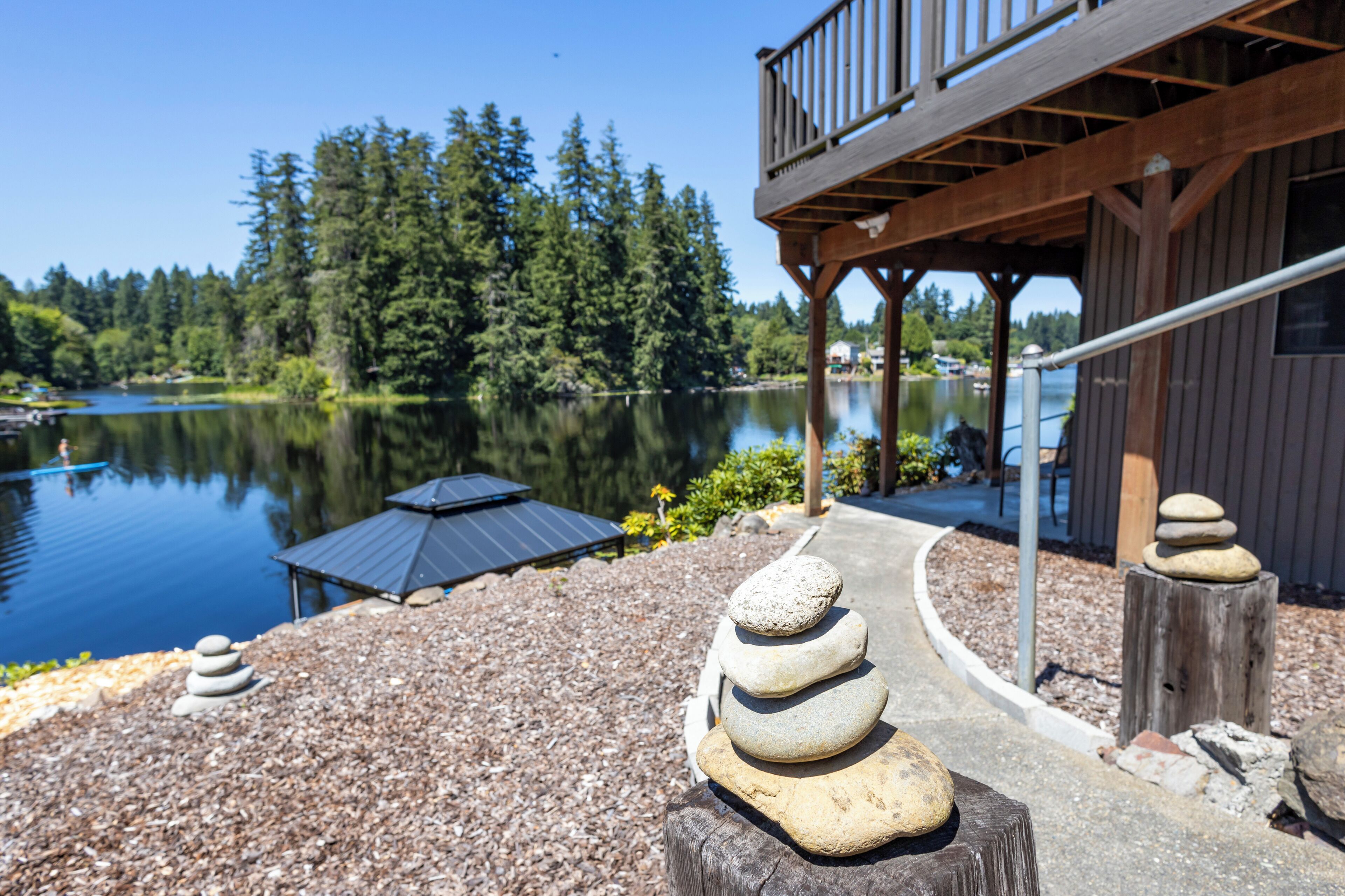 Une terrasse au bord du lac, dotée d’une rambarde en bois, d’un empilement de pierres et d’un parasol alimenté par énergie solaire.