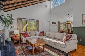A spacious living room with a large sectional sofa, a wooden coffee table, and a large window offering a view of the outdoors.