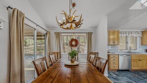 Une salle à manger avec une table en bois, des chaises, un lustre et une vue sur l’extérieur.