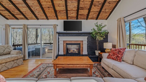 Un salon doté d’une cheminée, de poutres apparentes en bois au plafond, d’un canapé, d’une table basse et d’une vue sur l’extérieur grâce à une porte vitrée.