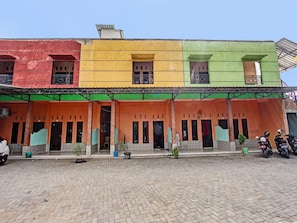A multi-story building with a colorful facade, multiple balconies, and a paved ground area with parked motorcycles. - Hotel O Homestay Bang HajiNearLapangan Penujak ( Inen Gonggang) (Praya)