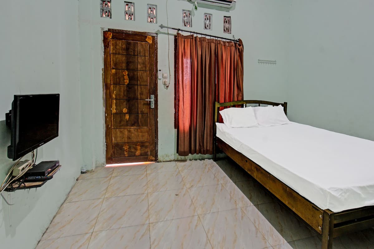 A room with a bed, a television, an air conditioner, and a door with curtains.