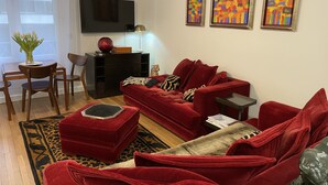A living room with a red sofa, a wooden coffee table, a leopard print rug, and a flat-screen TV mounted on the wall.