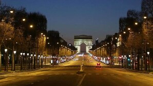 A wide street leading to a large, illuminated archway at dusk.