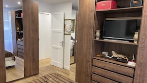 A bedroom with a wooden wardrobe, a bed, and a TV on a shelf.