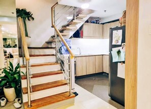 A modern kitchen with wooden flooring, a stainless steel refrigerator, and a staircase with a glass railing.