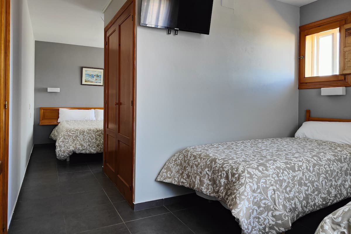 Une chambre avec deux lits, une télévision et une fenêtre.