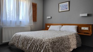 Uma cama bem arrumada com colcha estampada, cabeceira de madeira, quadro emoldurado na parede e janela com cortinas leves.