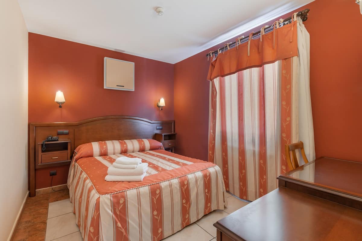 Une chambre à coucher avec un lit, des tables de chevet, une commode, un miroir et une fenêtre avec des rideaux.