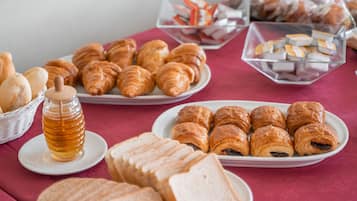 Une table de buffet proposant diverses pâtisseries, notamment des croissants et du pain, ainsi qu’un pot de miel.