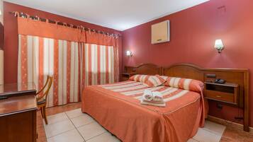 A hotel room with a bed, a desk, a chair, a nightstand, and a lamp.