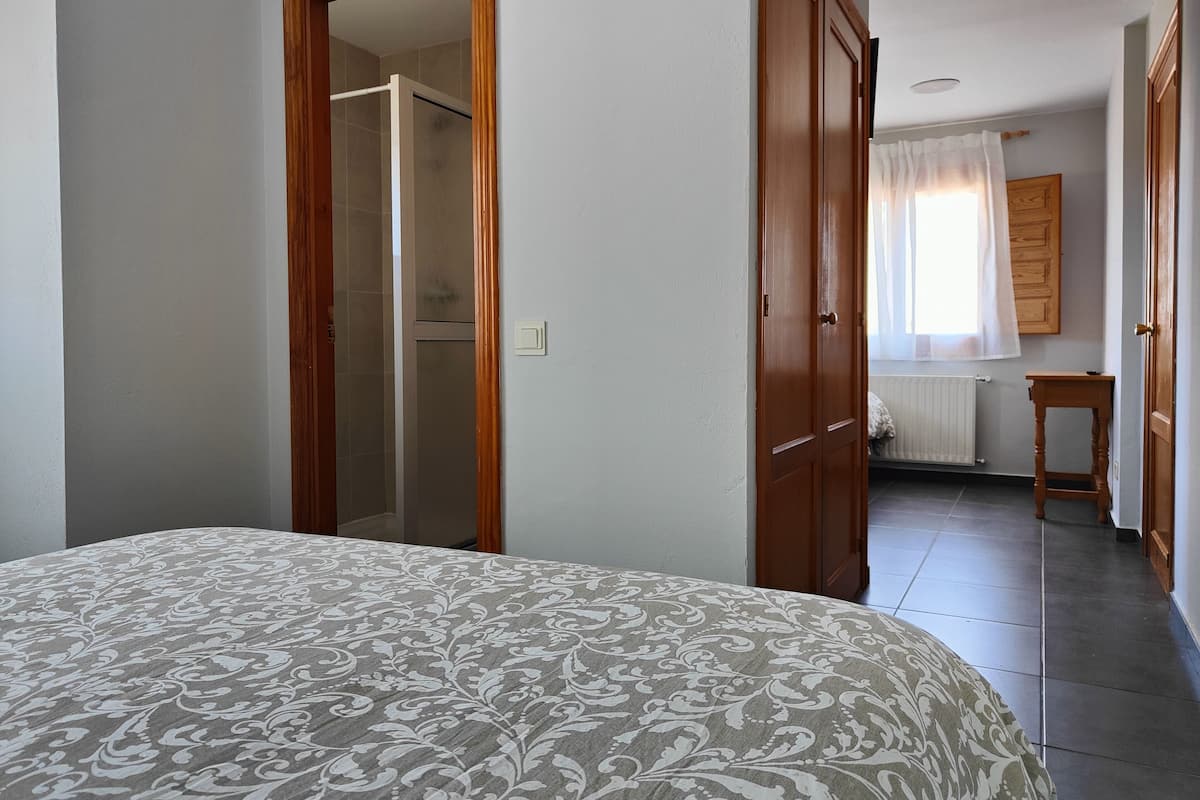 Une chambre à coucher avec un lit, une porte en bois, un radiateur et une fenêtre avec des rideaux.