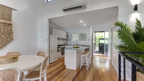 Una cocina moderna con armarios blancos, una isla central y un comedor con sillas de mimbre.
