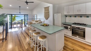 Una cocina moderna con una isla central, taburetes de bar, vistas al exterior y un área de comedor con balcón.