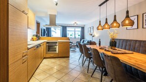 A modern kitchen with wooden cabinets, a built-in oven, and a dining area with a long wooden table and chairs. - Haus Obauer (Wagrain)