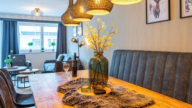 A modern living room with a wooden dining table, leather sofa, and pendant lighting. - Haus Obauer (Wagrain)