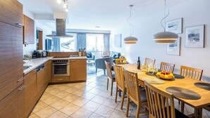 A modern kitchen with wooden cabinets, a central island, and a dining area with a wooden table and chairs. - Haus Obauer (Wagrain)