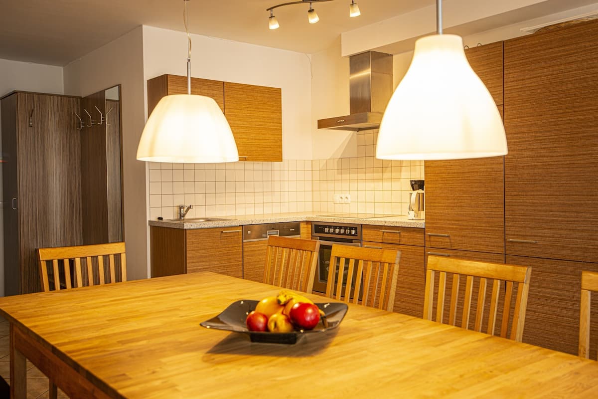 A modern kitchen with wooden cabinets, a dining table with chairs, and a fruit bowl on the table.