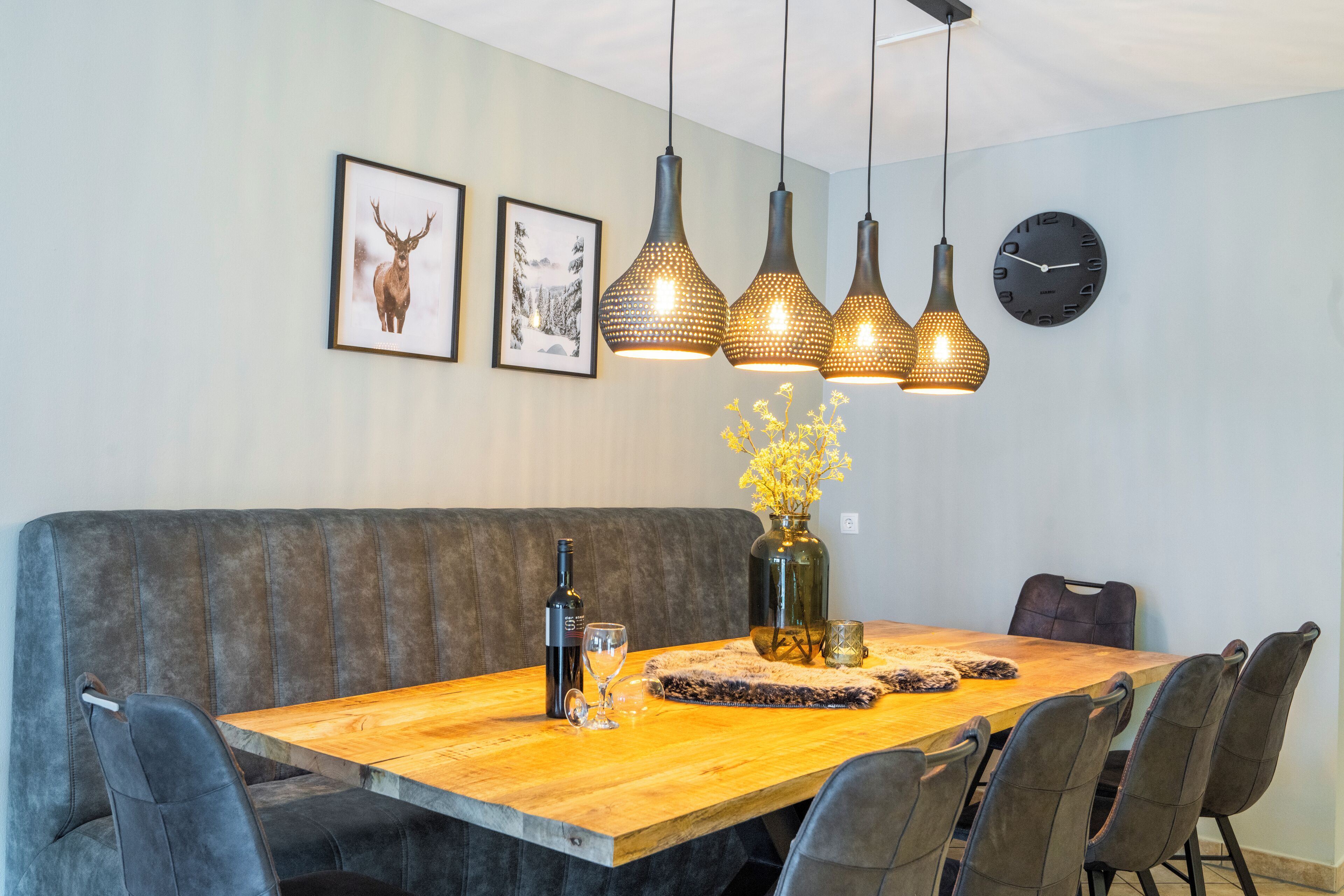 Uma área de refeições com mesa de madeira, bancos acolchoados e iluminação pendente.