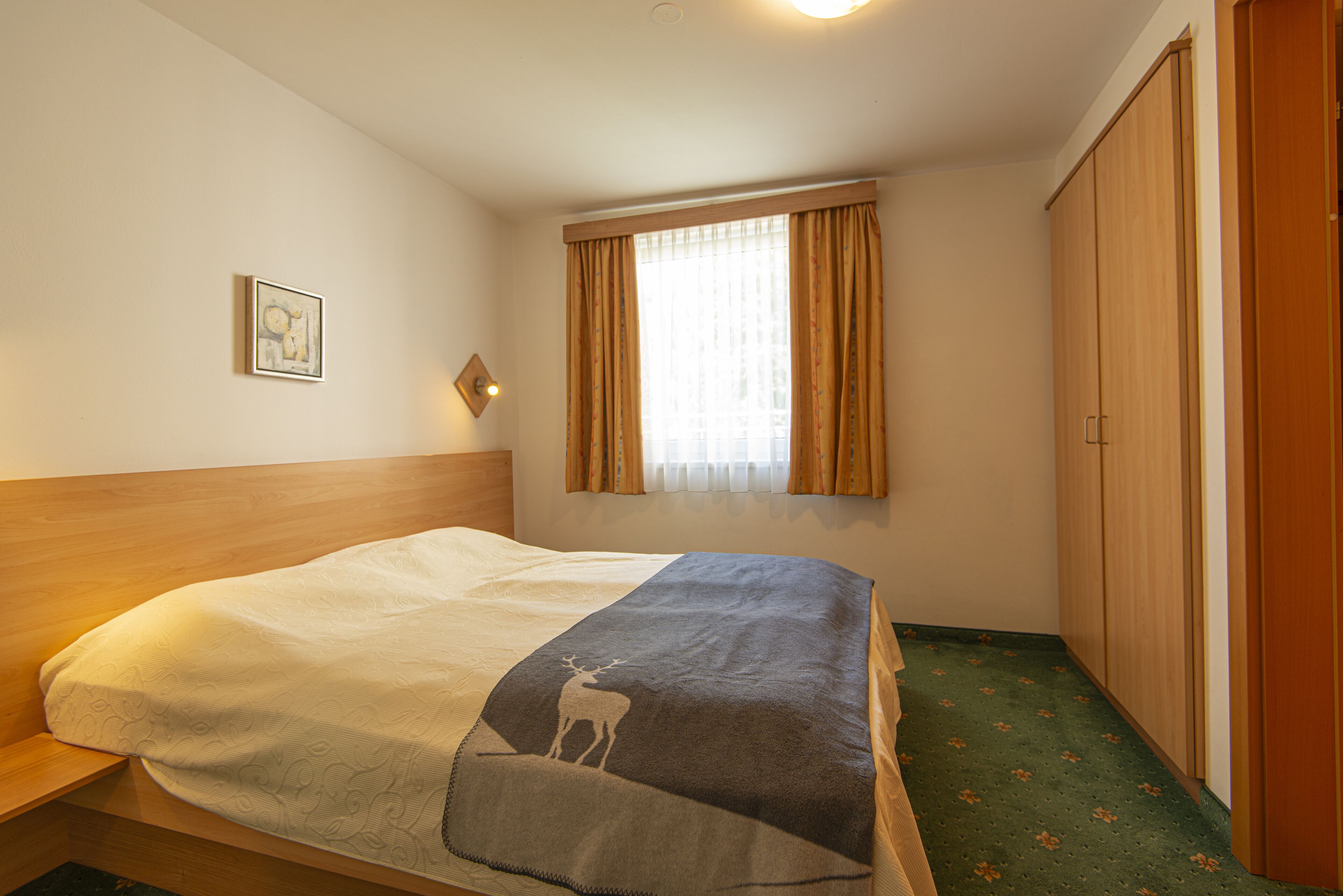 A bedroom with a bed, a window with curtains, a wardrobe, and a small picture on the wall.