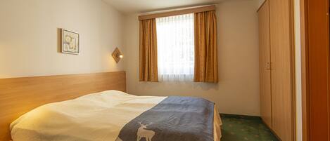 A bedroom with a bed, a window with curtains, a wardrobe, and a small picture on the wall.
