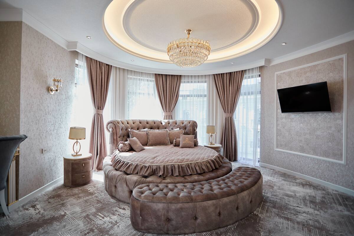 A luxurious bedroom with a large bed, a chandelier, and a television on the wall.