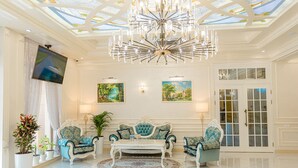 A spacious lobby with a chandelier, a television, two sofas, and a large rug. - Royal Hotel Samarkand (Samarkand)