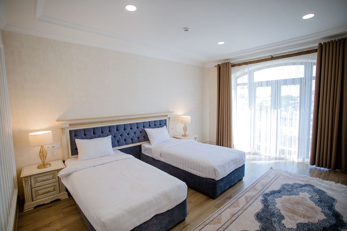 A hotel room with two beds, a large window with curtains, and a patterned rug.