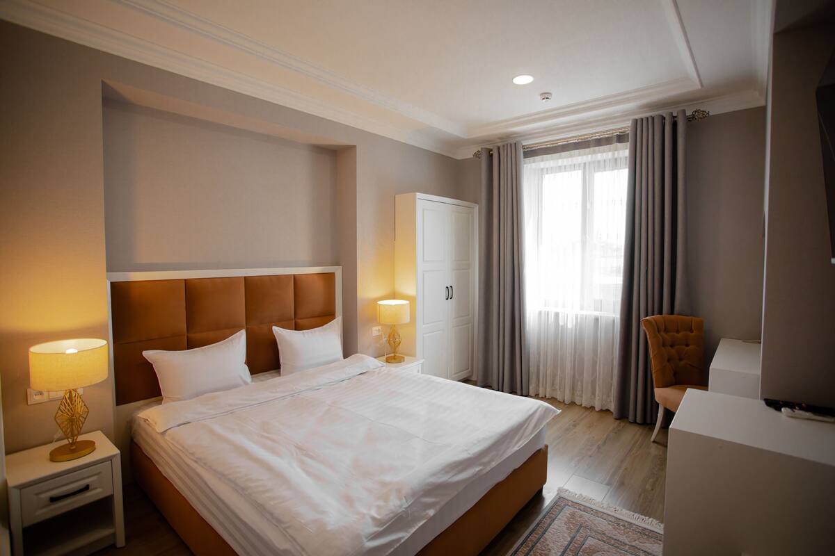 A hotel room with a large bed, bedside lamps, a wardrobe, a chair, and a television.