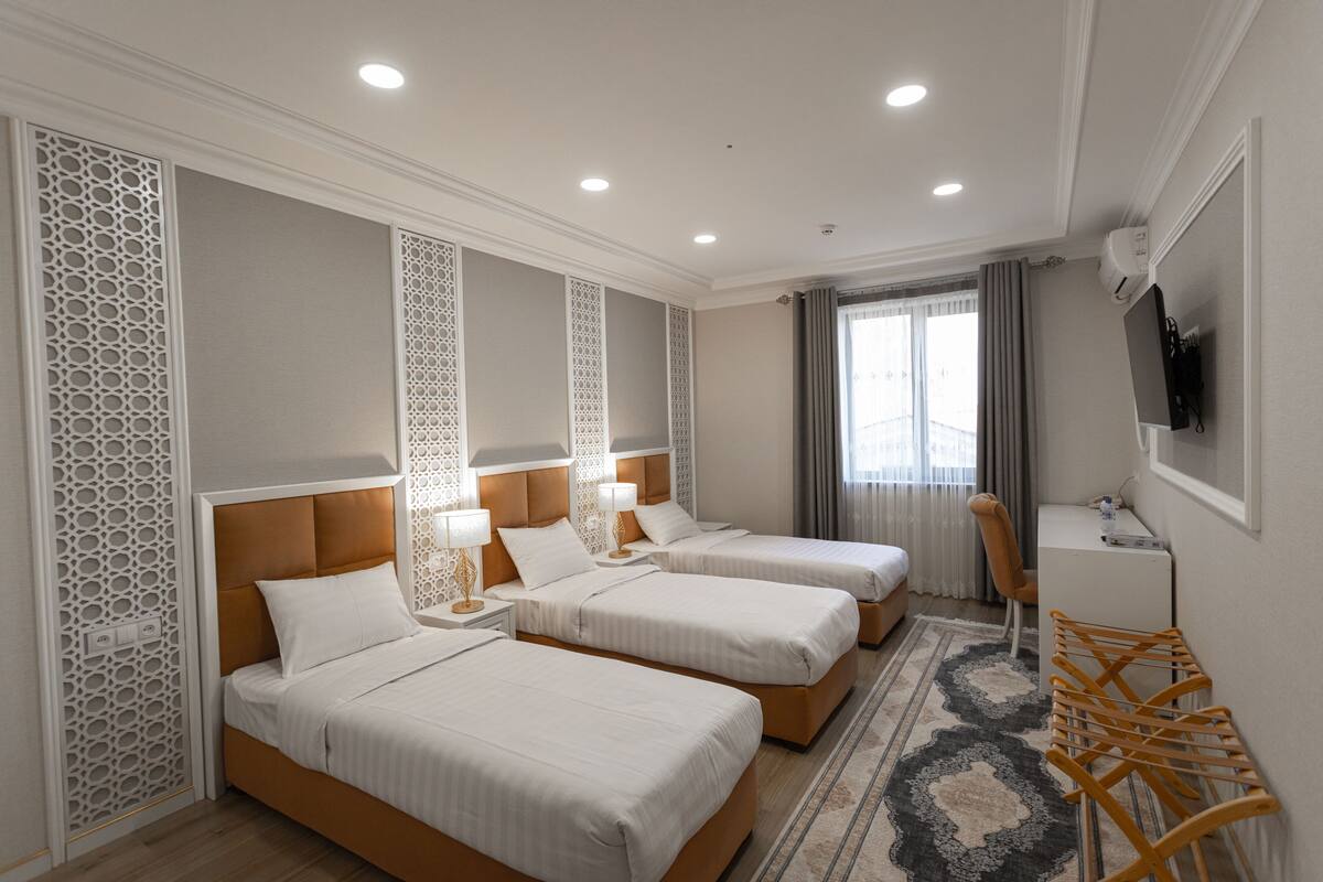 A hotel room with three single beds, a desk, a chair, and a TV on the wall.