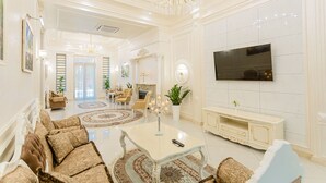 A spacious living room with a large TV, comfortable seating, and a chandelier. - Royal Hotel Samarkand (Samarkand)