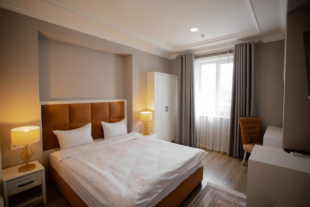 A hotel room with a large bed, bedside lamps, a wardrobe, a chair, and a television.