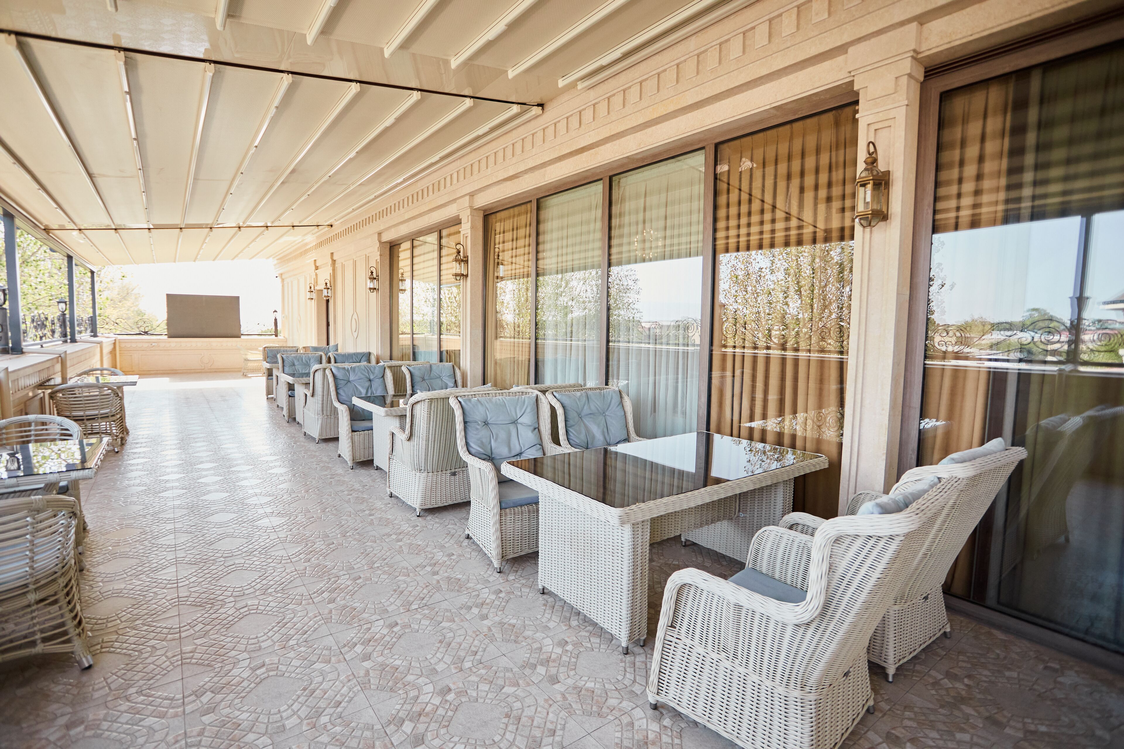 A covered outdoor seating area with wicker furniture and glass-top tables.