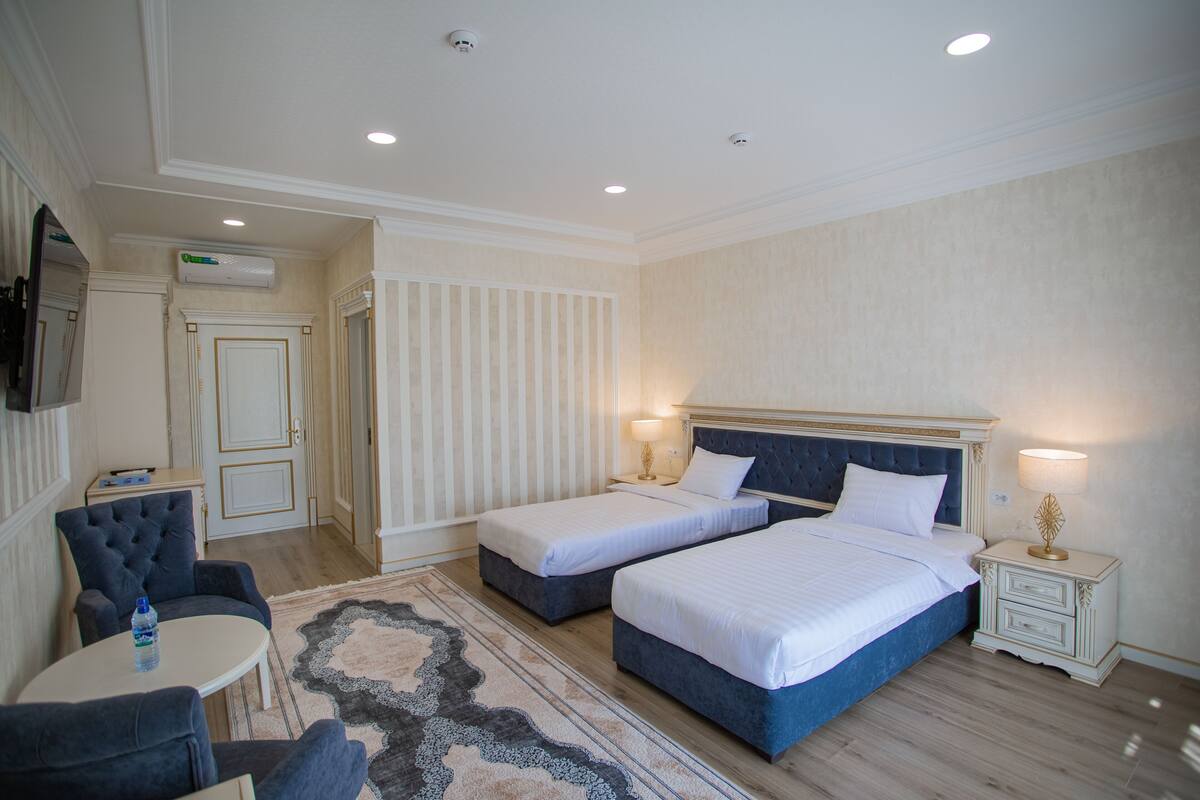 A hotel room with two beds, a sitting area with a table, and a TV mounted on the wall.