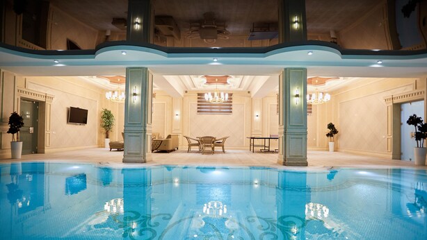 A large indoor swimming pool with a tiled floor, surrounded by a lounge area with chairs and a table, and a chandelier above. - Royal Hotel Samarkand (Samarkand)