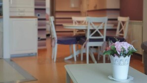 Ein Essbereich mit weißen Stühlen und einem Tisch, eine weiße Vase mit Blumen und ein Holzboden.