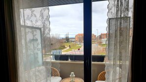 Ein Balkon mit Korbmöbeln und einer Laterne, mit Blick auf eine Straße mit Gebäuden und einem Park.