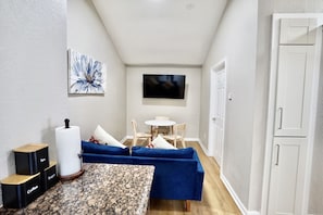 A compact living space with a blue sofa, a small dining table, a coffee machine, and a TV mounted on the wall. - Unique 1 Bedroom House in San Jose (San Jose)