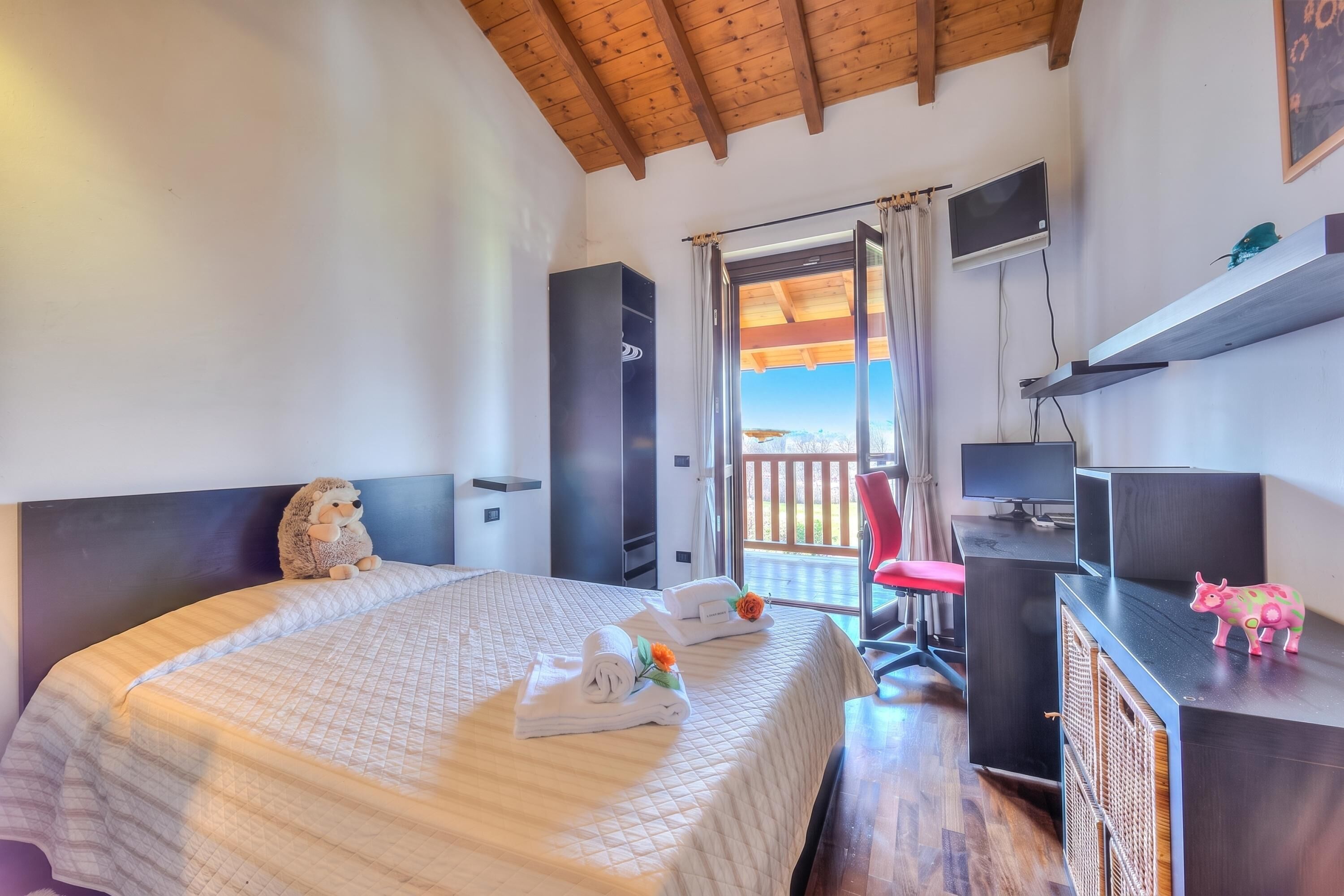 A bedroom with a bed, a desk, a chair, a TV, and a balcony.