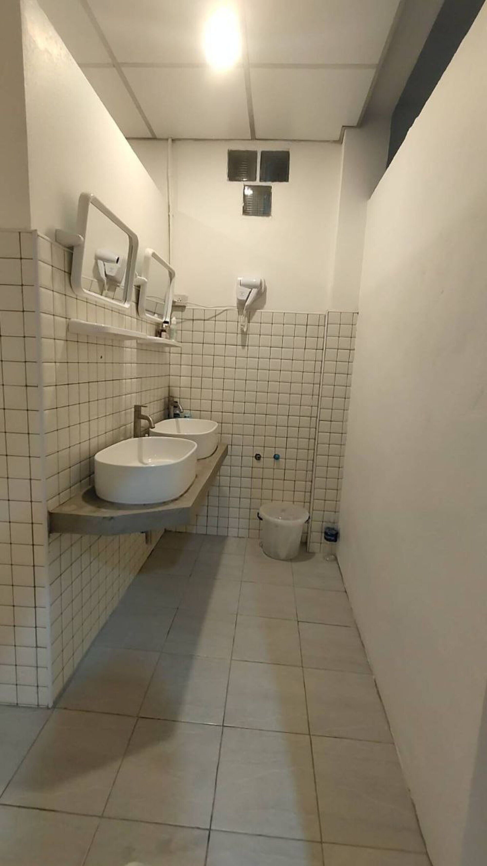 A small, tiled bathroom with two sinks, a toilet, and a mirror.