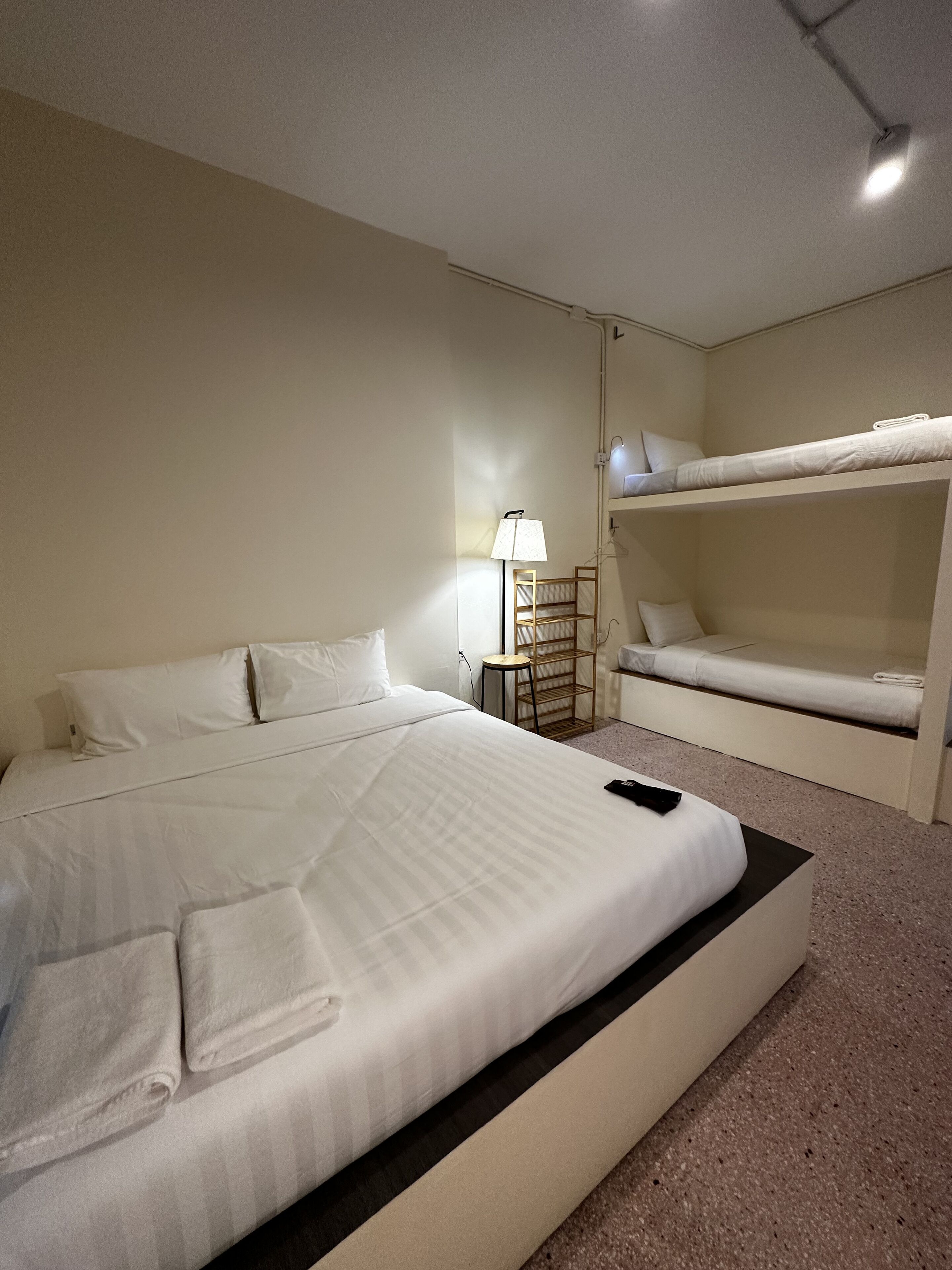 Habitación de hotel con una cama grande, una mesita de noche con lámpara y una cama litera en la esquina.
