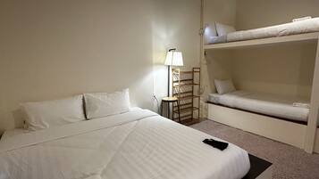 Habitación de hotel con una cama grande, una mesita de noche con lámpara y una cama litera en la esquina.